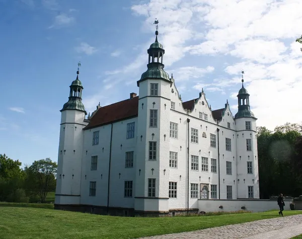 Historisches Schloss in Stormarn mit weißer Fassade und vier markanten Türmen bei klarem Himmel.