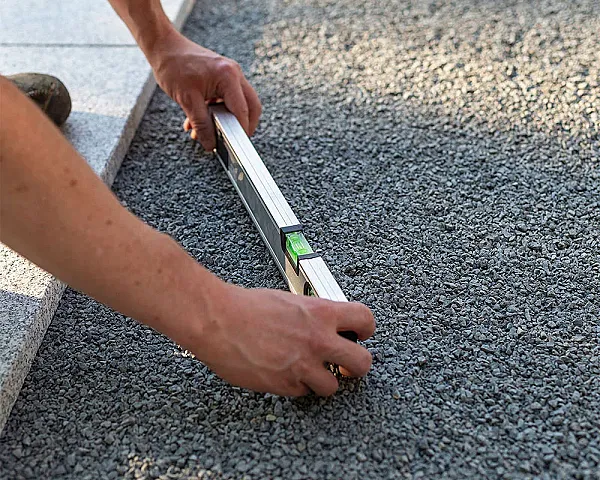 Hände nivellieren Basaltsplitt mit einer Wasserwaage auf Terrasse, Hünten GmbH.