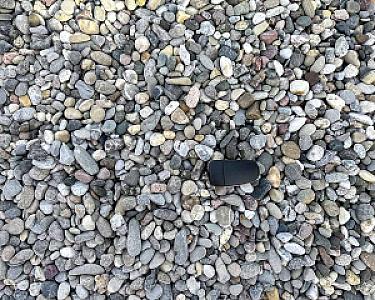 Drainagekieshaufen mit einer kleinen schwarzen Schaufel darauf, Kiesel in verschiedenen neutralen Tönen.