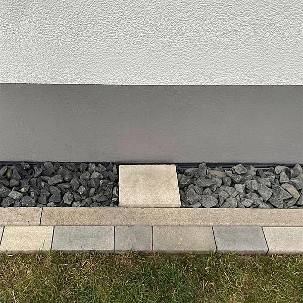 Basaltsplitt neben einer Hauswand mit quadratischer Steinplatte und Randsteinbegrenzung.