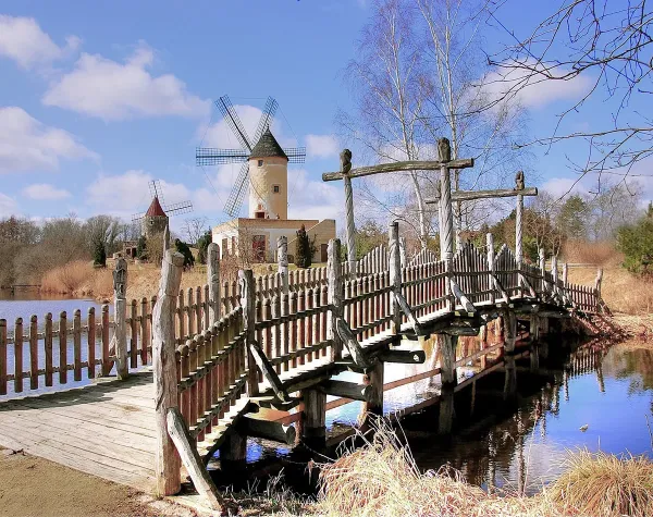 Windmühlenpark in Gifhorn mit Holzbrücke über einen Teich, klare Himmel und Winterlandschaft.