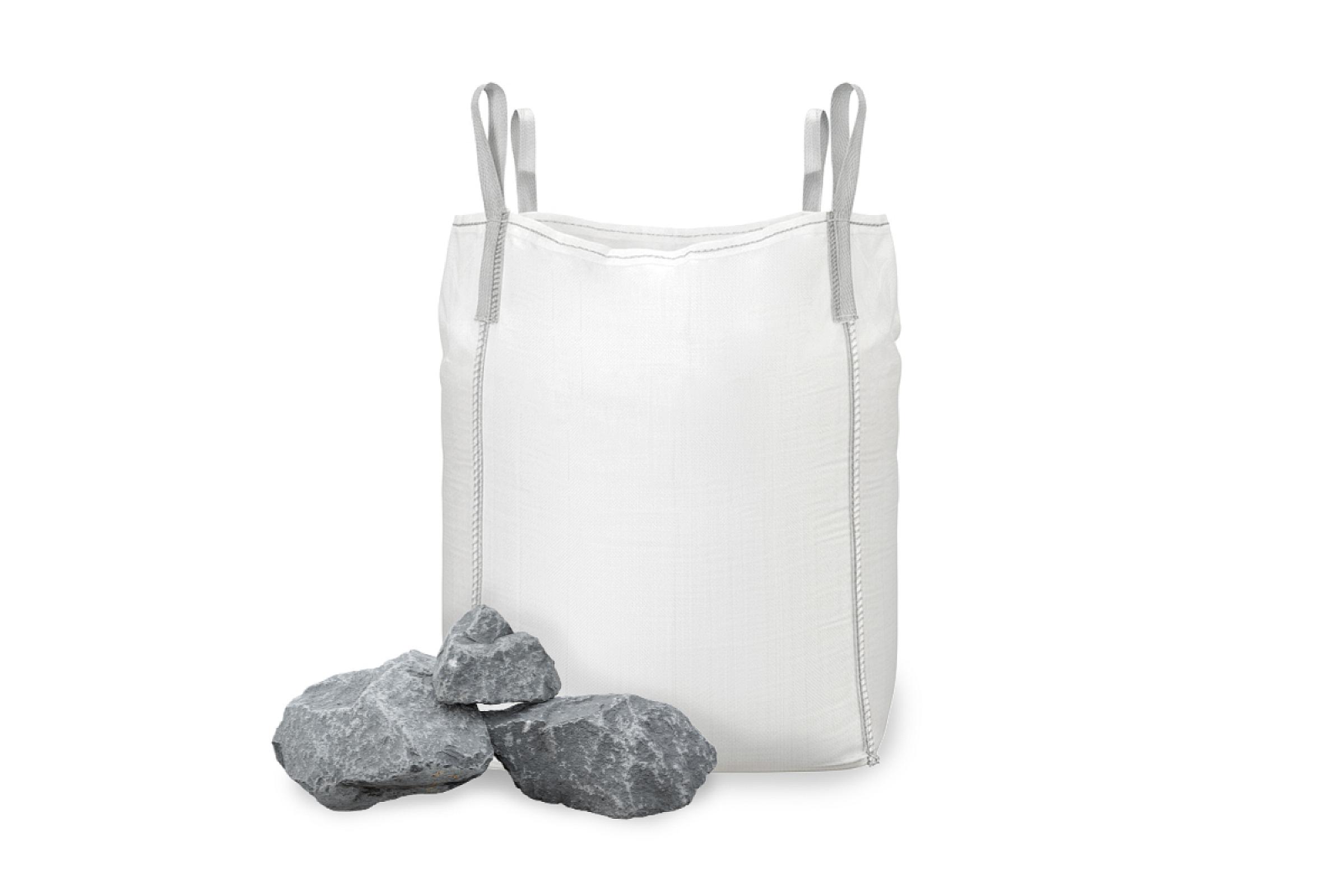 Großer weißer Big Bag mit Basalt-Wasserbausteinen, einige Steine liegen daneben.