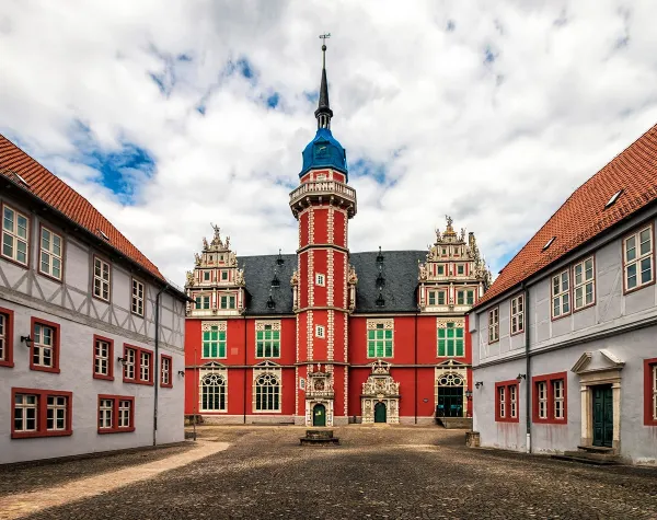 Historisches Gebäude mit roter Fassade und Fachwerkhäusern in Helmstedt bei bewölktem Himmel.