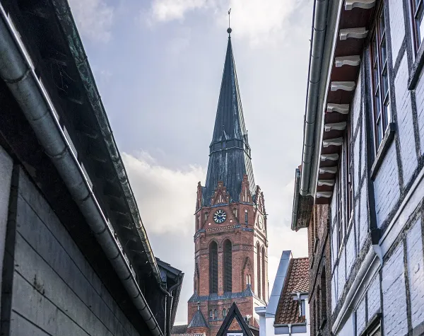 Historisches Gebäude und Kirchturm in Nienburg (Weser), umgeben von Fachwerkhäusern unter wolkigem Himmel.
