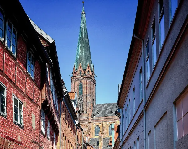 Straßenszene in Lüneburg mit Kirchturm im Hintergrund bei klarem Himmel, von historischen Backsteinhäusern gesäumt.