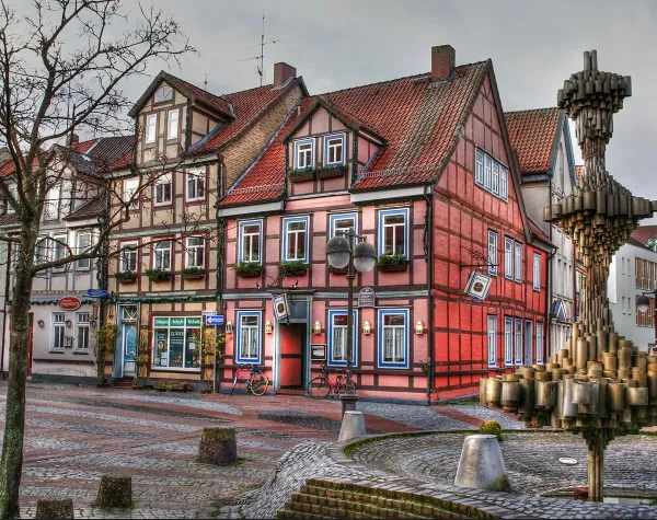 Fachwerkhäuser in Uelzen mit verzierten Fassaden und einem modernen Brunnen im Vordergrund. Kopfsteinpflasterstraße.