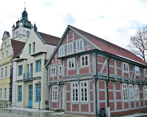 Historisches Fachwerkhaus in Verden mit markanten Mustern, daneben modernes Gebäude und Kirchturm im Hintergrund.
