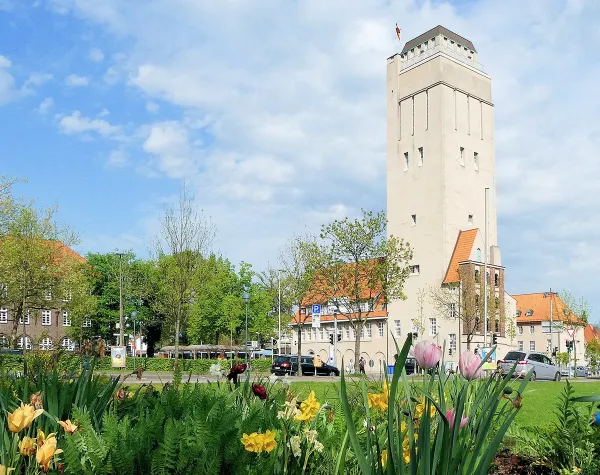 Delmenhorster Wasserturm mit umliegenden historischen Gebäuden und blühenden Blumen im Vordergrund.
