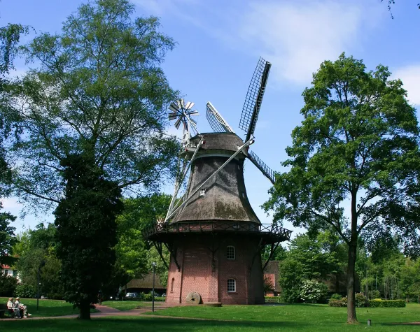 Historische Windmühle im Ammerland, umgeben von grünen Bäumen und Wiese bei leicht bewölktem Himmel.