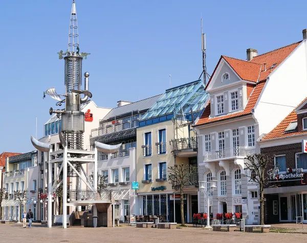 Mehrstöckige Gebäude und Skulptur auf dem Marktplatz in Aurich, sonniger Tag.
