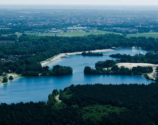 Landschaft mit Seen, Grünflächen und einem entfernten Blick auf Emsland, von bewaldeten Flächen umgeben.