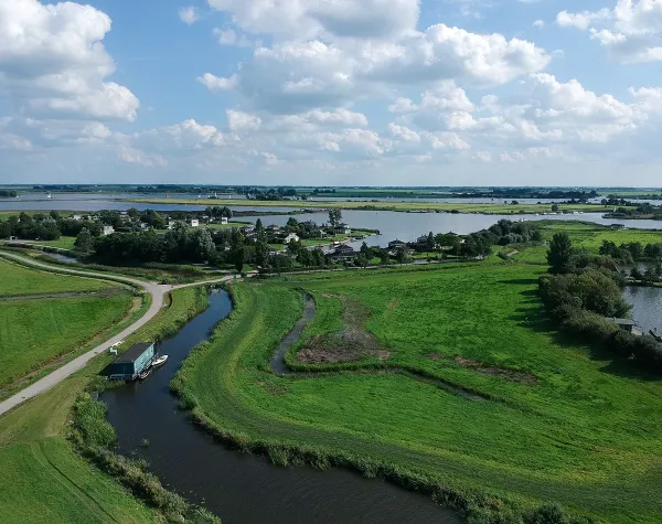 Landschaft mit grünen Wiesen, kleinen Wasserstraßen und Häusern unter einem wolkigen Himmel in Friesland.