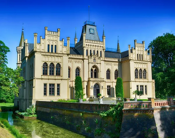 Historisches Schloss mit neugotischen Türmen und Wassergraben, umgeben von Bäumen im Landkreis Leer.