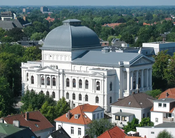 Kuppelgebäude in Oldenburg, umgeben von grünen Bäumen und roten Dächern, darunter das Staatstheater.