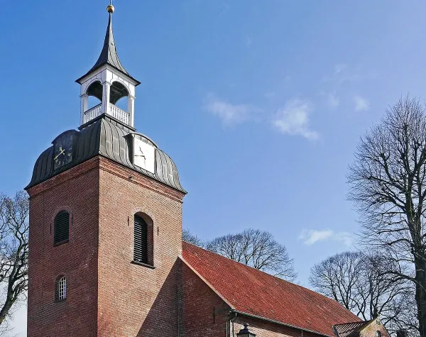 Backsteinkirche in Wittmund mit Turm und blauem Himmel; umgeben von kahlen Bäumen.