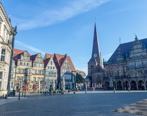 Historischer Marktplatz in Bremen mit Rathaus, Kirchen und Café unter blauem Himmel.