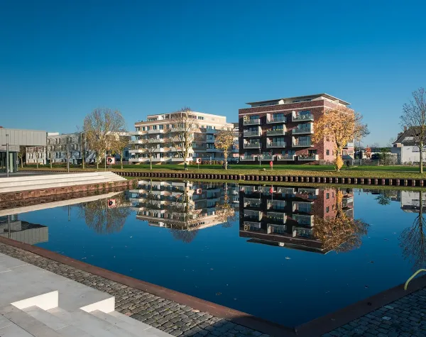 Moderne Gebäude spiegeln sich in einem ruhigen Gewässer in Kleve, umgeben von Herbstbäumen und klarem Himmel.