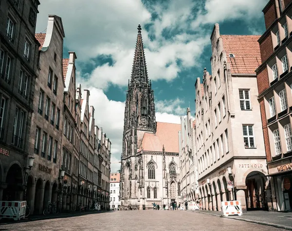 Historisches Stadtbild von Münster mit imposanter Kirche und historischen Gebäuden unter blauem Himmel.