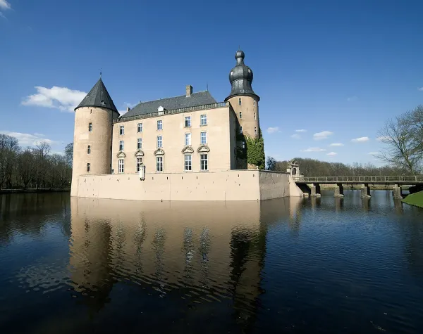 Wasserburg mit Turm in Borken, umgeben von Wassergraben, blauer Himmel und Brücke im Hintergrund.