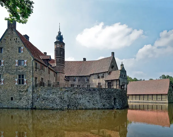 Historisches Schloss an einem Wassergraben in Coesfeld an einem sonnigen Tag, mit einem Turm und umgebenden Gebäuden.