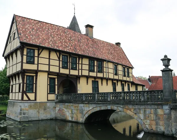 Fachwerkhaus in Steinfurt mit rotem Ziegeldach, Brücke über Wassergraben im Vordergrund.