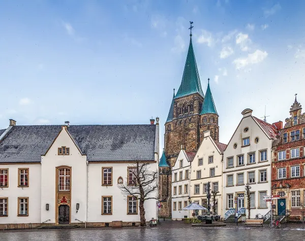Historische Gebäude am Marktplatz von Warendorf mit Kirche im Hintergrund bei bewölktem Himmel.