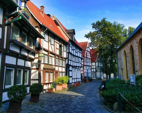 Fachwerkhäuser in enger, gepflasterter Gasse in Gütersloh, flankiert von Bäumen und einem historischen Gebäude.