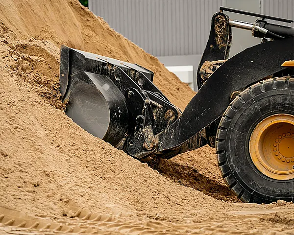Bagger schaufelt gewaschenen Mauersand in einer industriellen Umgebung.