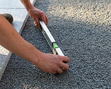 Person ebnet grauen Basaltsplitt 2-8 mm mit Wasserwaage, für Bauvorhaben oder Gartenarbeit.