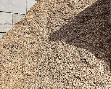 Lose Holzhackschnitzel in einem großen Haufen auf einer Betonfläche. Schatten fällt teilweise über den Haufen.