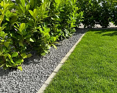 Lavamulch in Anthrazit als Beetumrandung neben grüner Hecke und Rasenfläche.