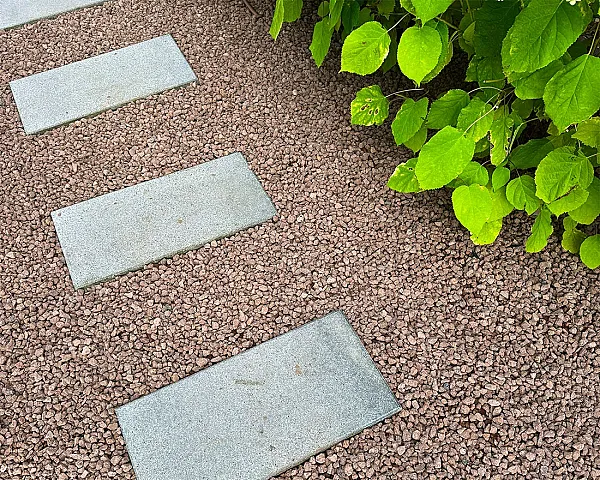 Gartenweg mit grauen Trittsteinen, umgeben von rot-braunem Lavamulch und grünem Blattwerk.