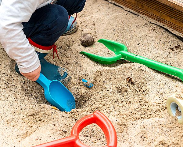 Kind spielt im Sandkasten mit bunten Sandspielzeugen, Sand stammt von Florikomp Erden & Substrate GmbH.