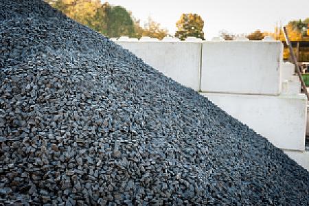Dunkelgrauer Basaltsplitt aufgetürmt vor hellen Betonblöcken im Außenbereich.