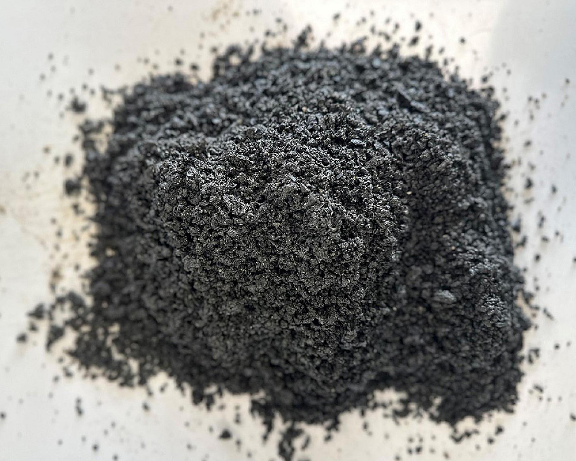 Ein Haufen feiner, dunkler Basaltsand von Volz und Herbert GmbH auf hellgrauem Hintergrund.