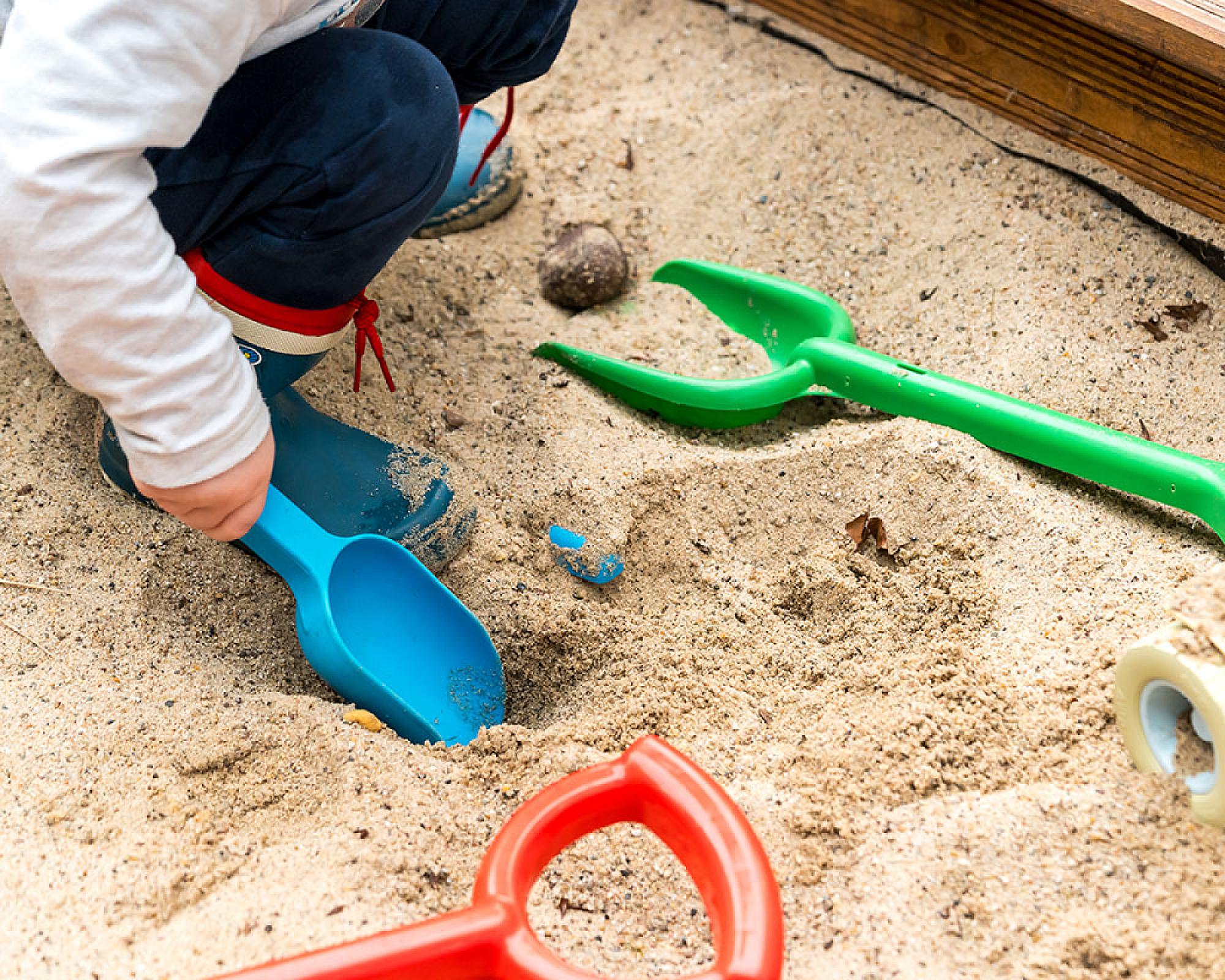 Kind spielt mit bunten Sandspielzeugen in einem Sandkasten. Zertifizierter Spielsand von Volz und Herbert GmbH.