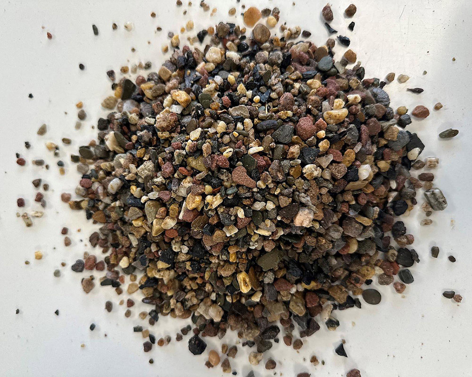 Ein Haufen bunter Fallschutzkies aus unterschiedlichen Mineralien auf einer weißen Fläche.