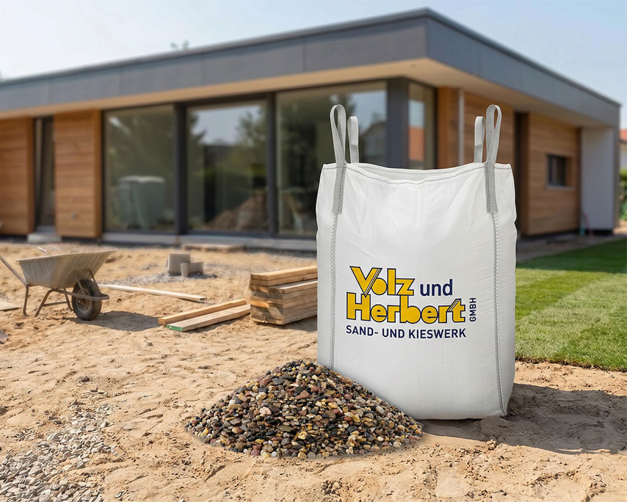 Großer Bigbag mit Filterkies von Volz und Herbert GmbH auf Baustelle vor modernem Gebäude.