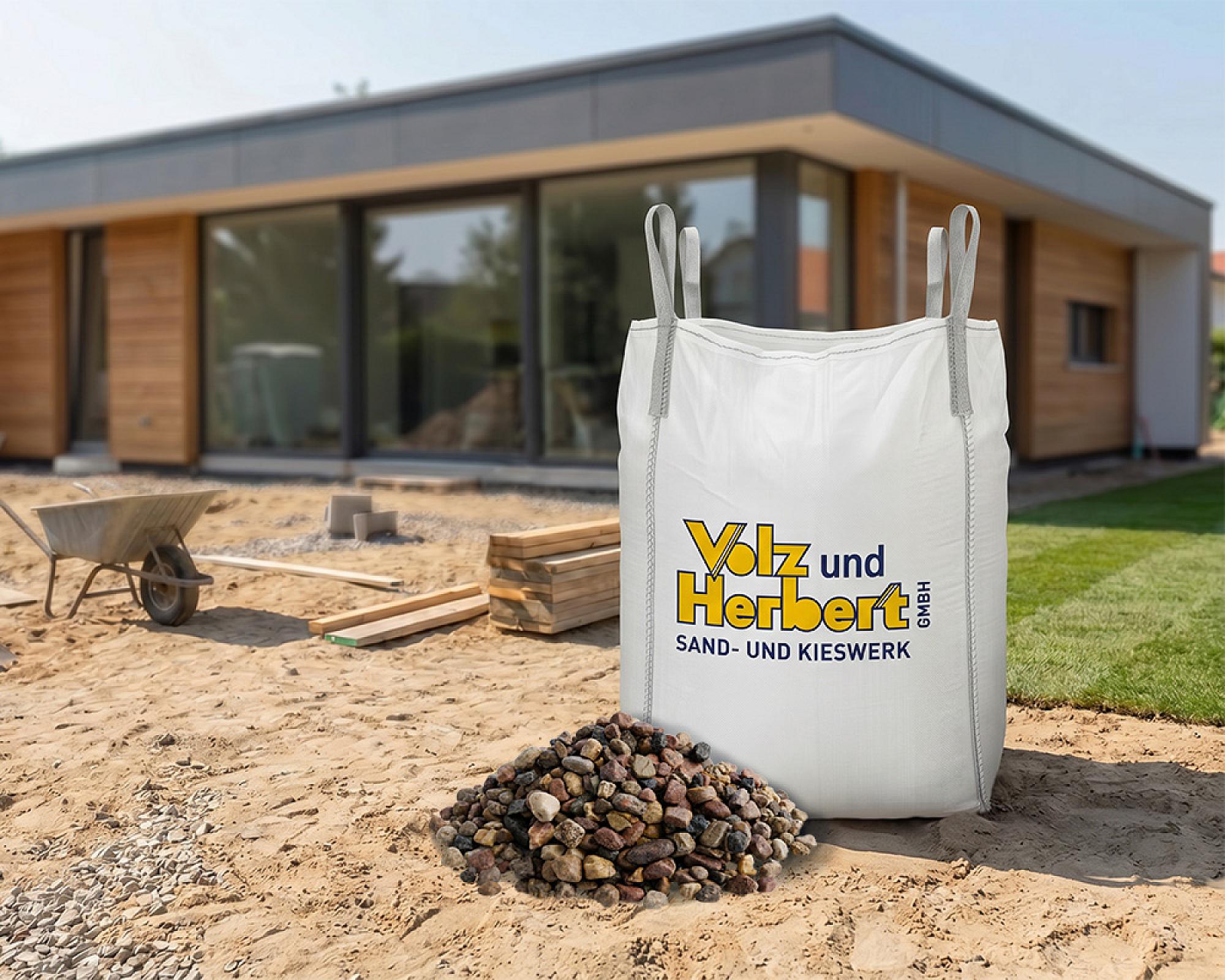 Großer Bigbag von Volz und Herbert GmbH mit Filterkies vor modernem Gebäude auf Baustelle.