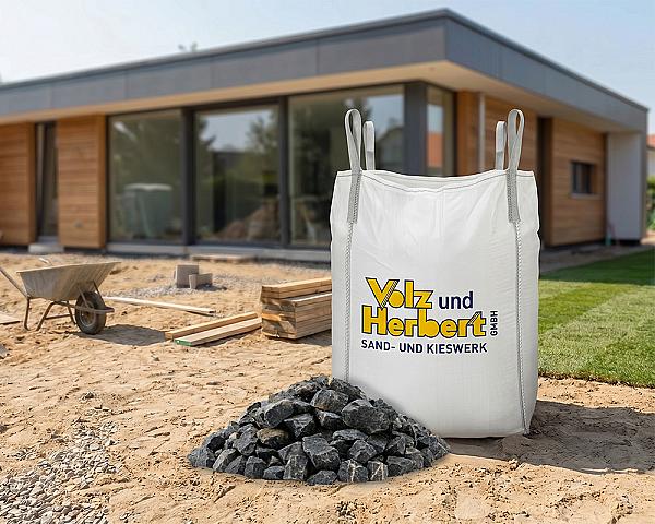 Big Bag mit Basaltsplitt 8-16 mm vor modernem Gebäude auf Baustelle, Marke Volz und Herbert GmbH.