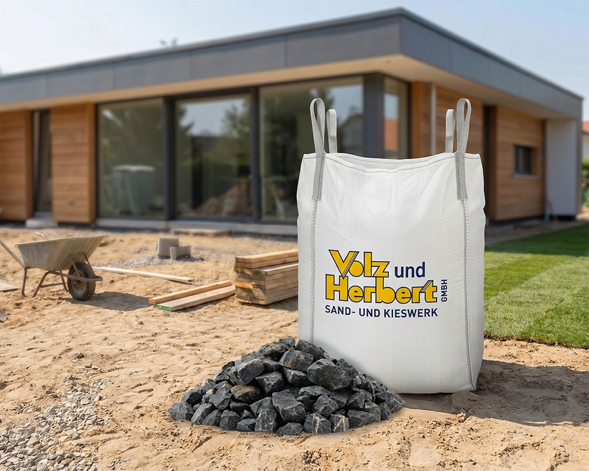 Big Bag mit Basaltsplitt 8-16 mm vor modernem Gebäude auf Baustelle, Marke Volz und Herbert GmbH.