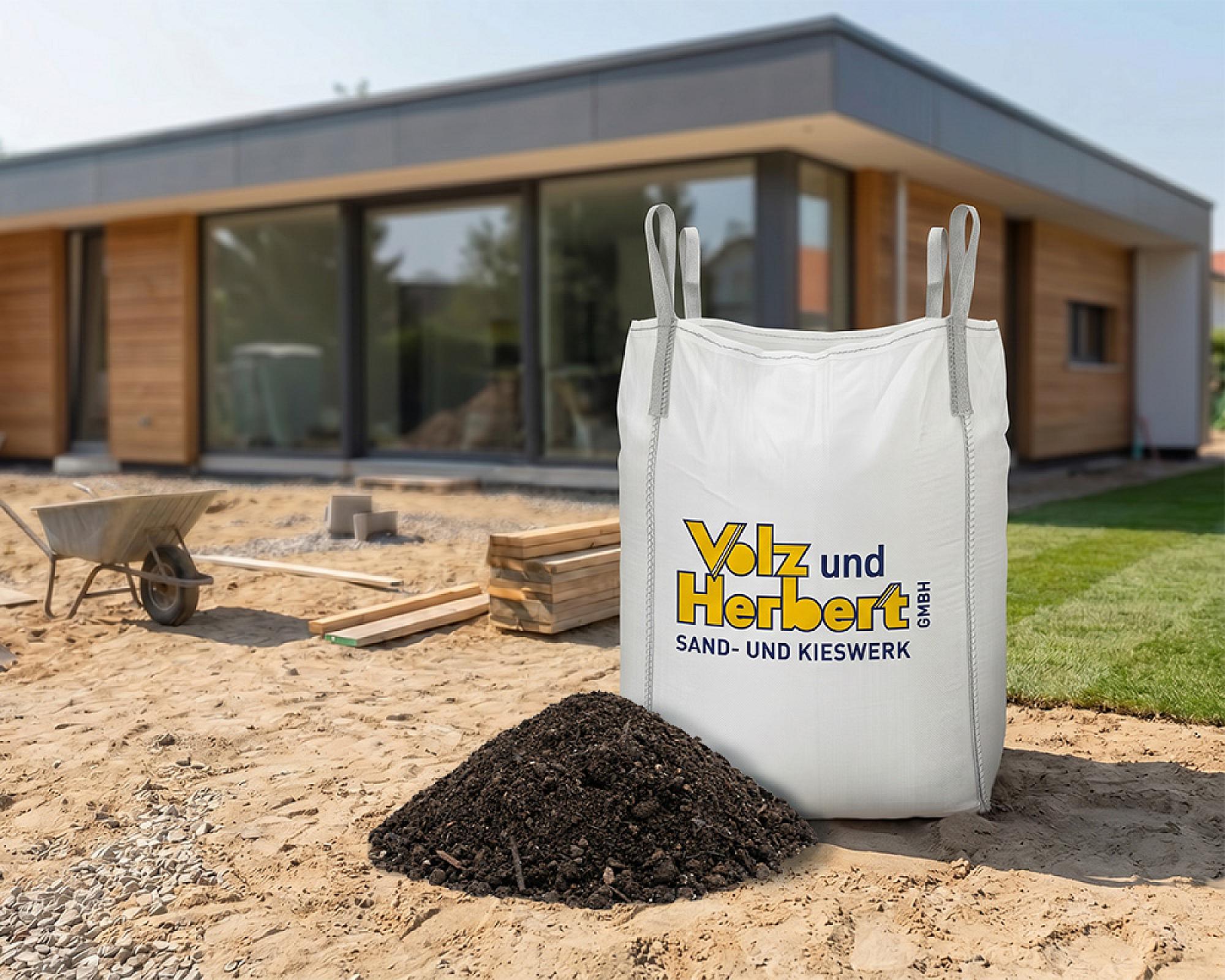 Großer weißer Big Bag der Volz und Herbert GmbH mit Erde gefüllt, steht vor einem modernen Holzhaus im Garten.
