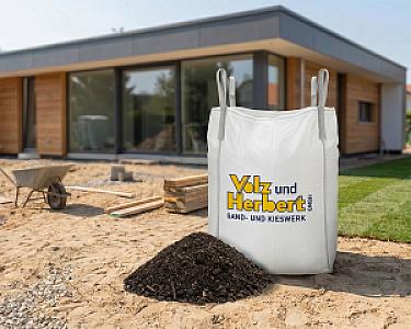 Großer weißer Big Bag der Volz und Herbert GmbH mit Erde gefüllt, steht vor einem modernen Holzhaus im Garten.