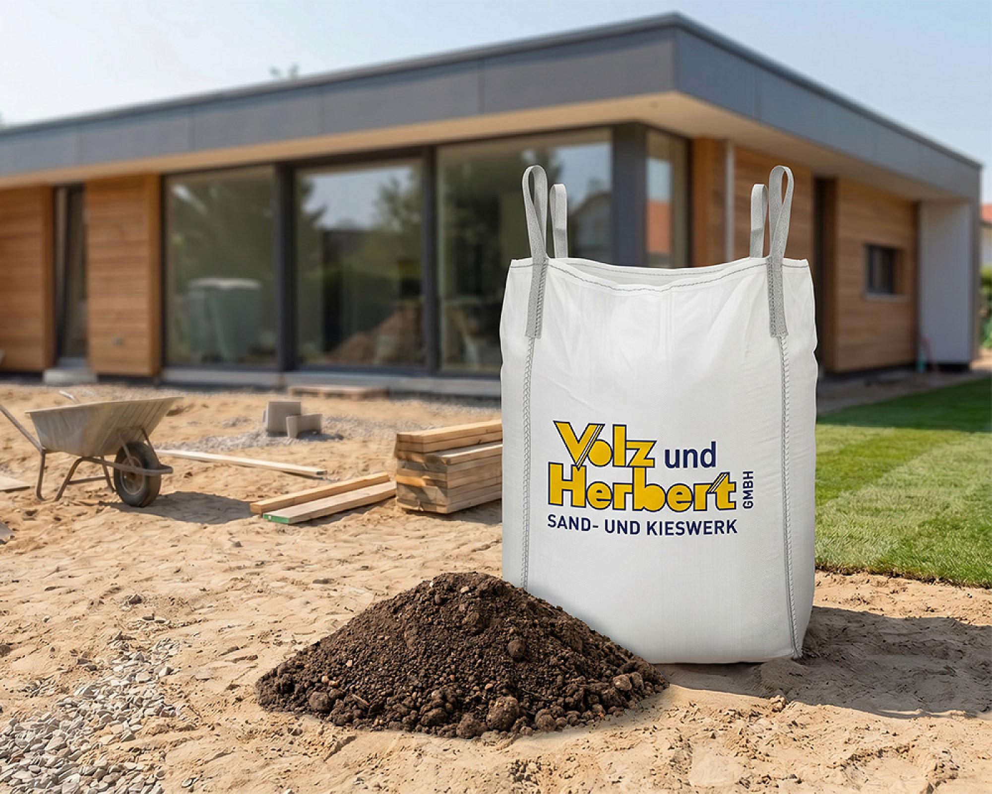 Großer Bigbag mit Volz und Herbert-Logo vor modernem Holzhaus auf Baustelle, gefüllt mit gesiebtem Oberboden.