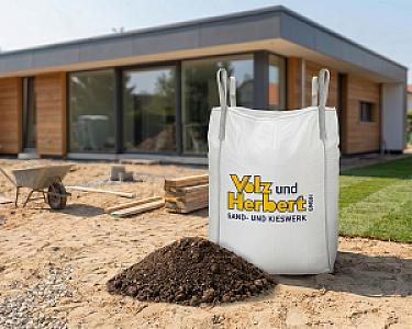 Großer Bigbag mit Volz und Herbert-Logo vor modernem Holzhaus auf Baustelle, gefüllt mit gesiebtem Oberboden.