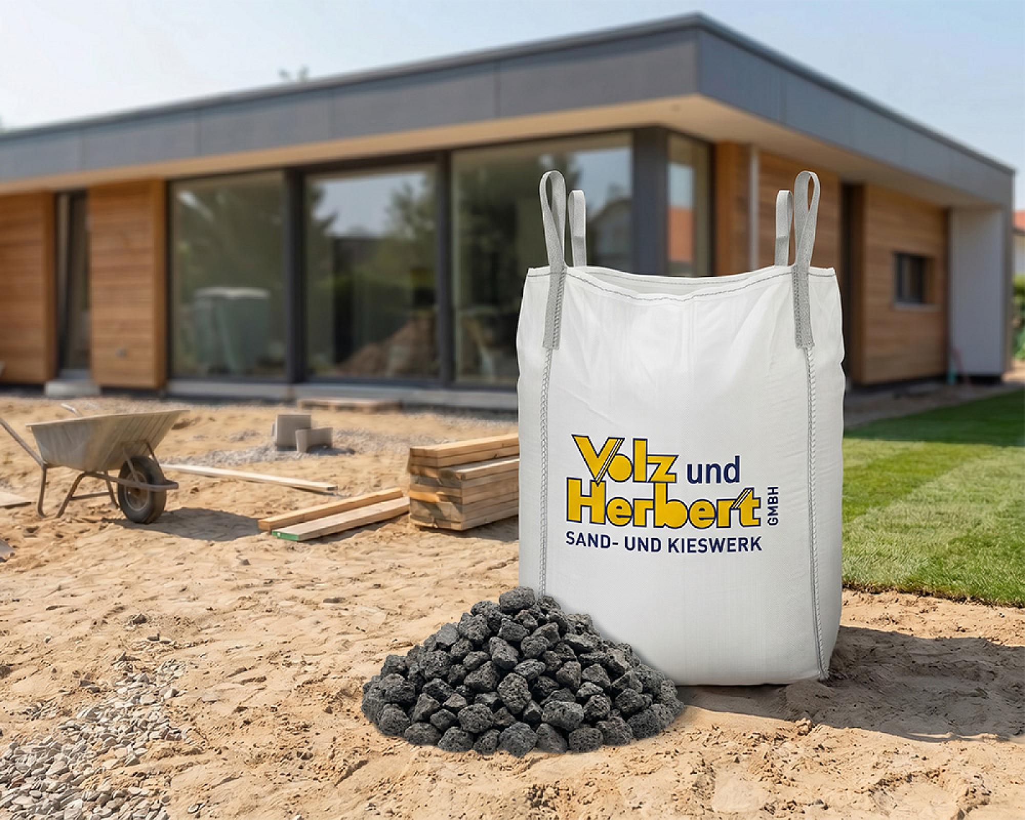 Big Bag mit Basaltschotter vor einem modernen Haus und Baustelle.