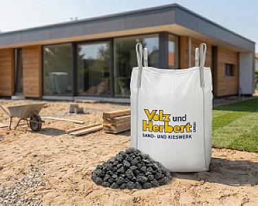 Big Bag mit Basaltschotter vor einem modernen Haus und Baustelle.