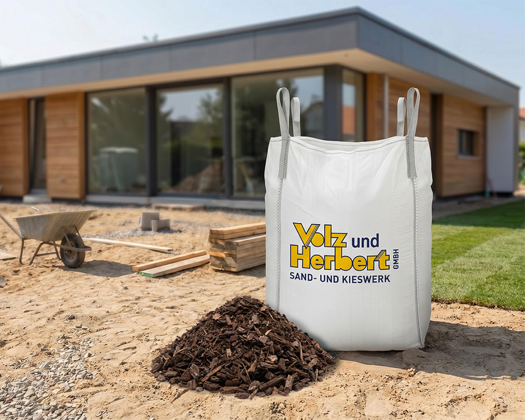 Großer Big Bag mit grobem Rindenmulch von Volz und Herbert GmbH auf Baustelle vor modernem Haus.