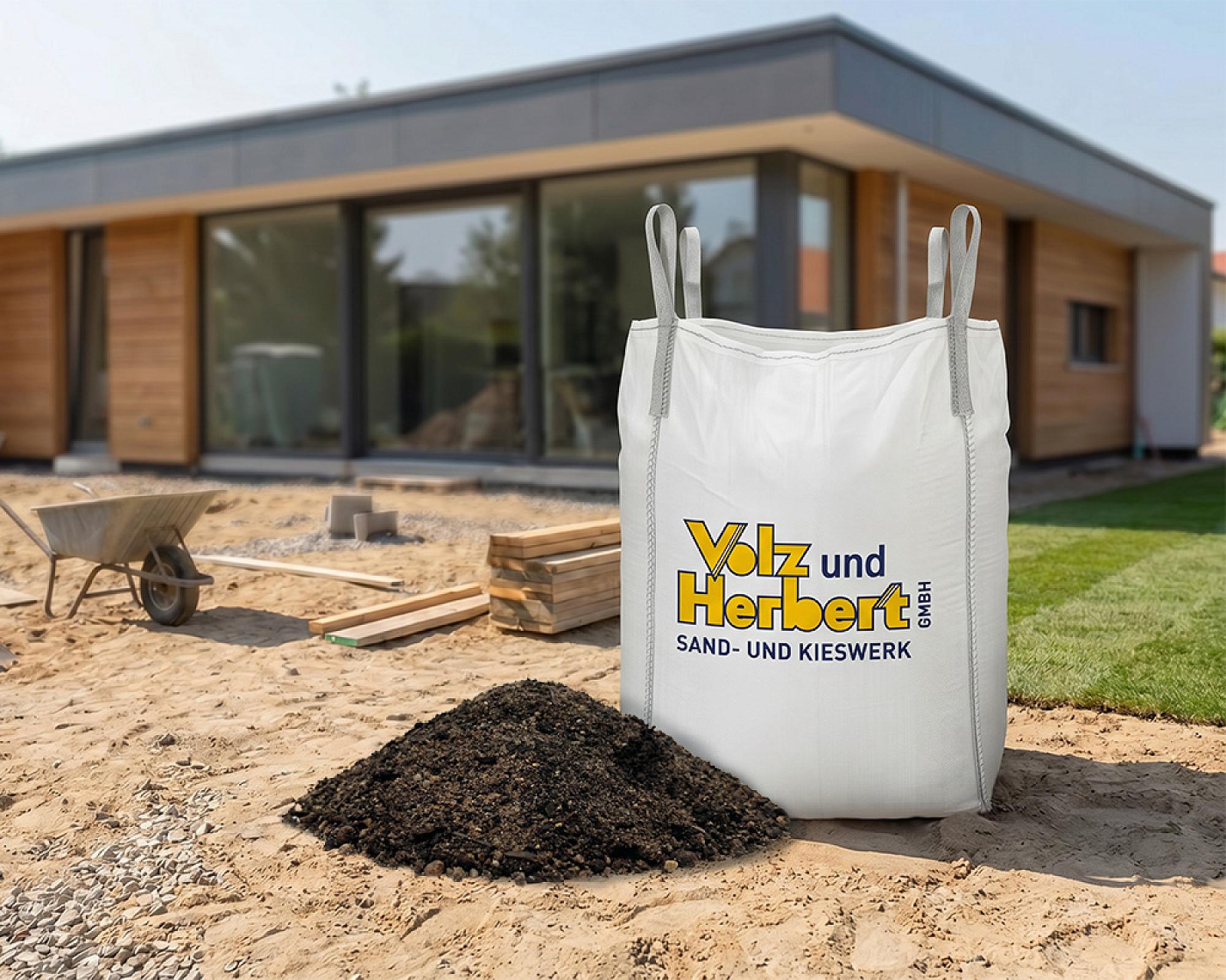 Großer Big Bag mit Sand-Kompost-Gemisch vor modernem Haus auf Gartenbaustelle.