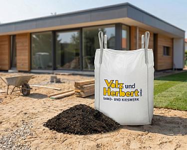 Großer Big Bag mit Sand-Kompost-Gemisch vor modernem Haus auf Gartenbaustelle.